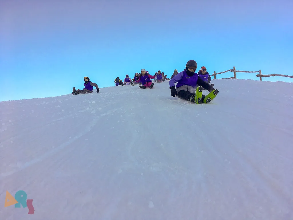 Jugendliche sitzen in der Dämmerung auf einer Schneekuppe.